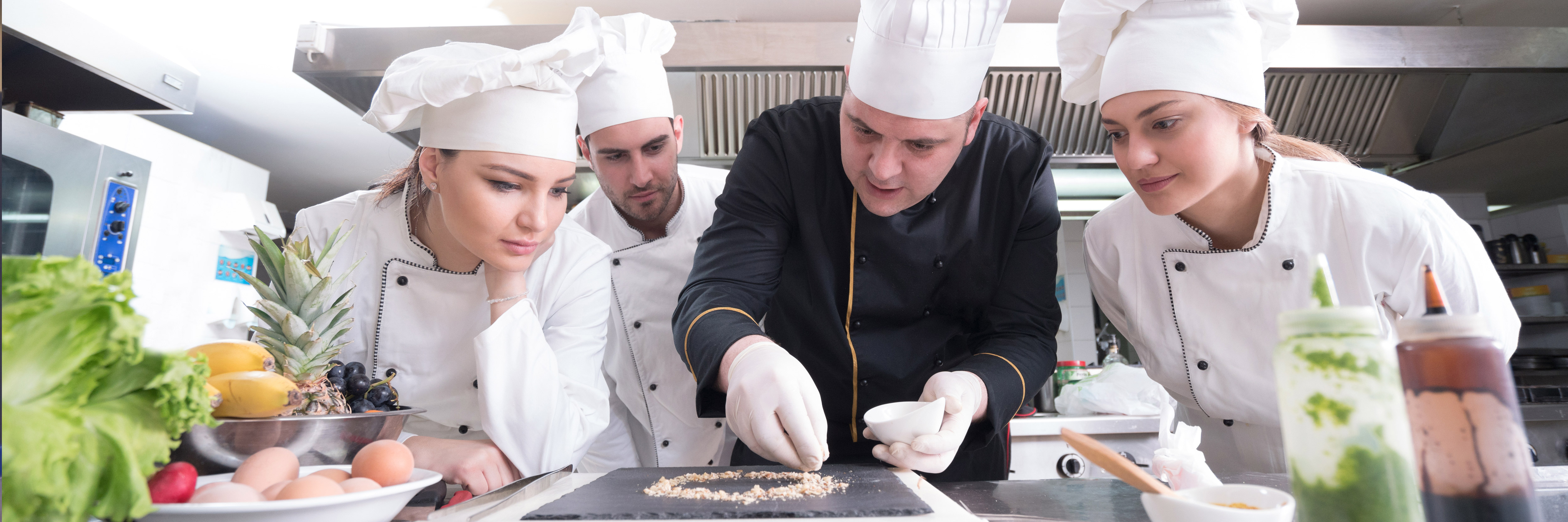 a group of Commis Chef apprentices watching a chef prepare a dish